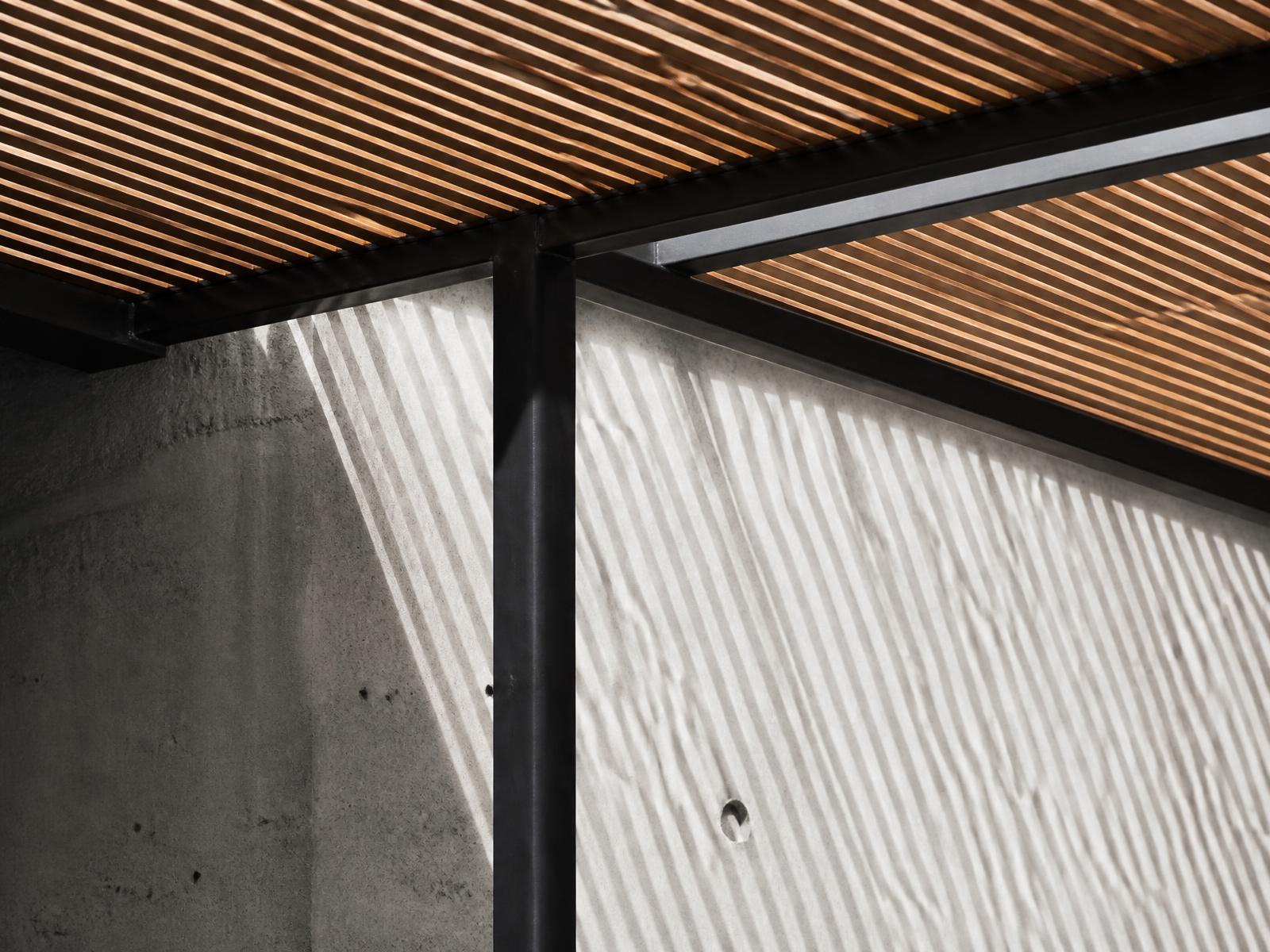 Black steel frame with timber slats casting shadows on a concrete wall
