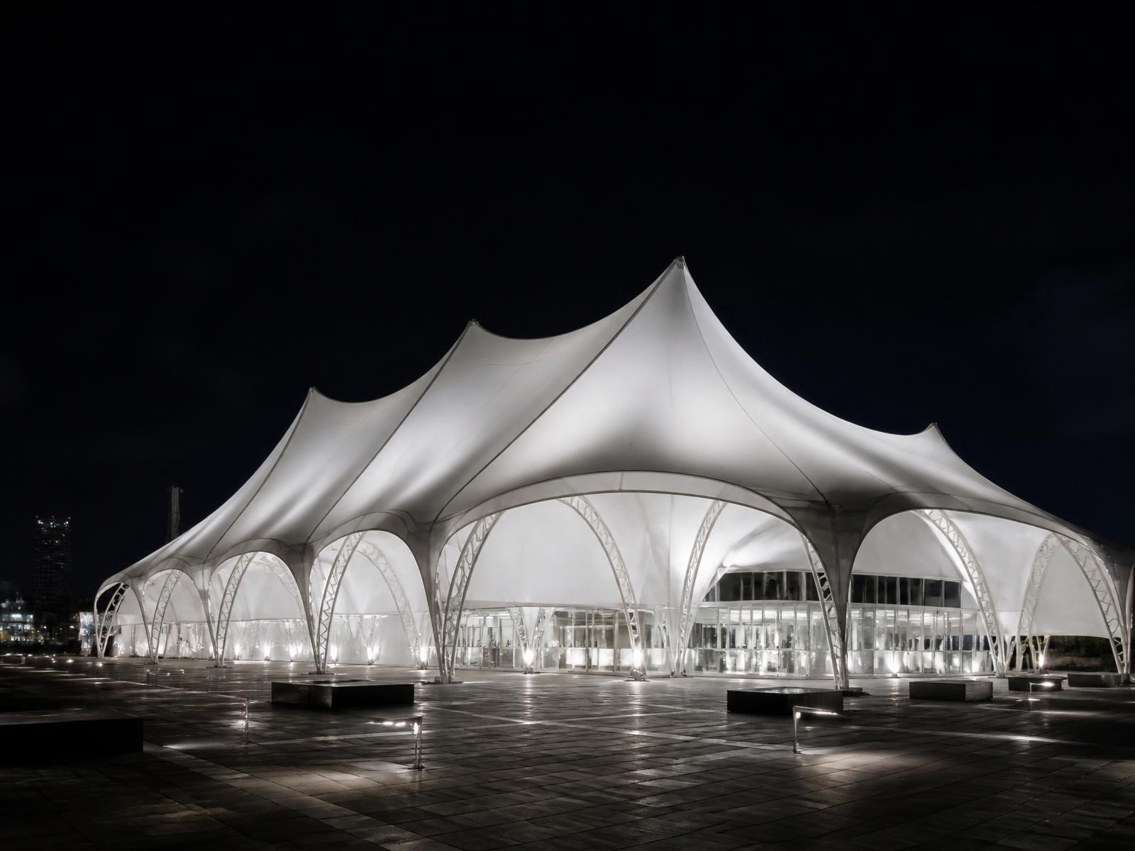 Illuminated temporary event pavilion on a plaza at night
